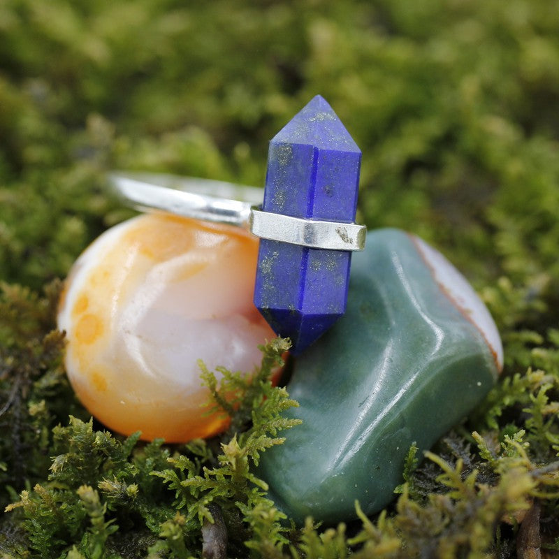 A lapis lazuli crystal point ring on 2 tumbled stones surrounded by greenery