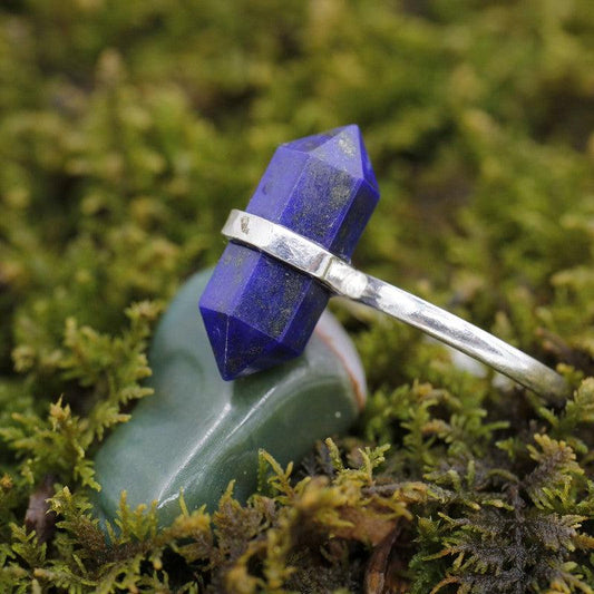 A lapis lazuli crystal ring set in silver on top of a green tumbled stone, on a bed of moss